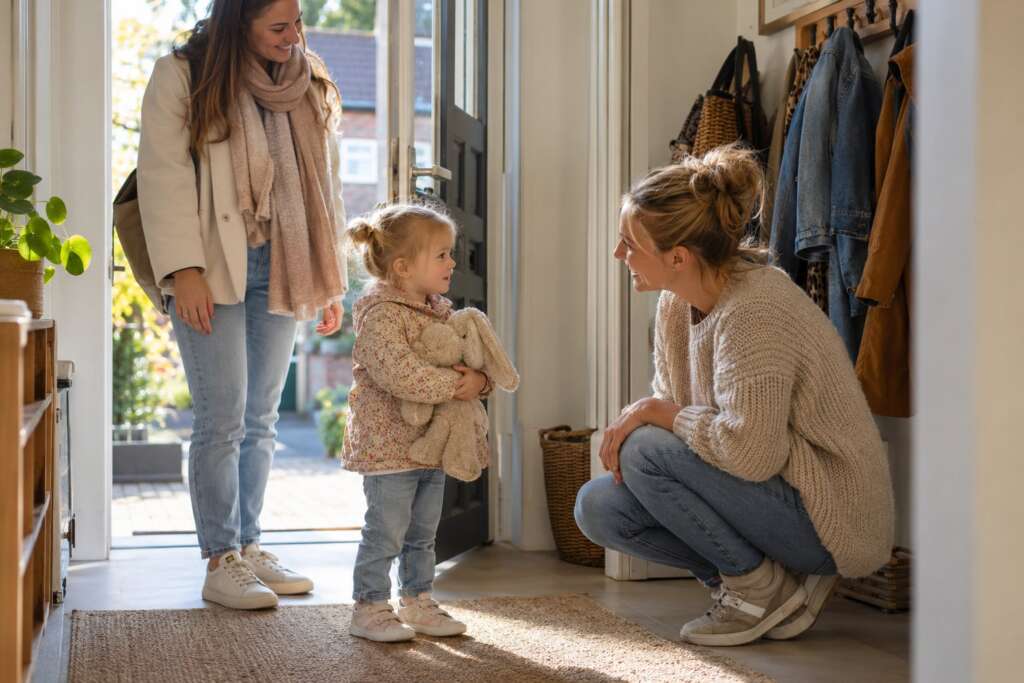 Moeder brengt haar dochtertje met knuffel naar de gastouder, die op ooghoogte zit