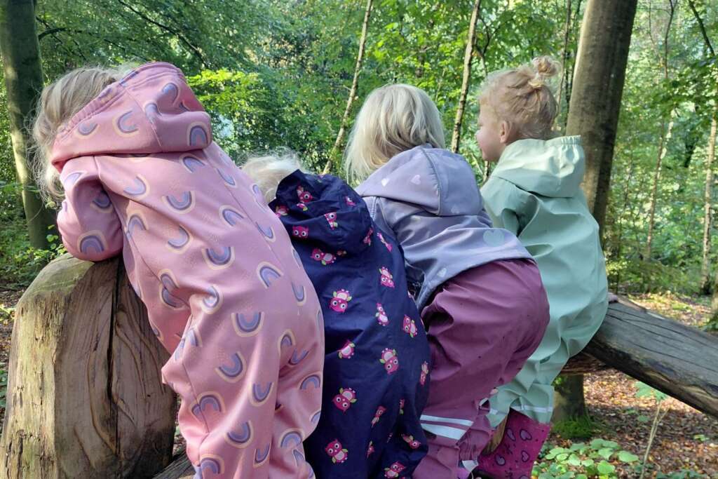 Vier peuters in regenpakken klimmen samen op een houten speeltoestel in het bos